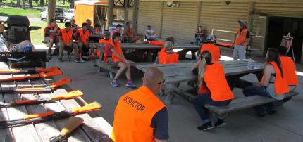 Two hunter education instructors with approximately 20 students in an outdoor setting.